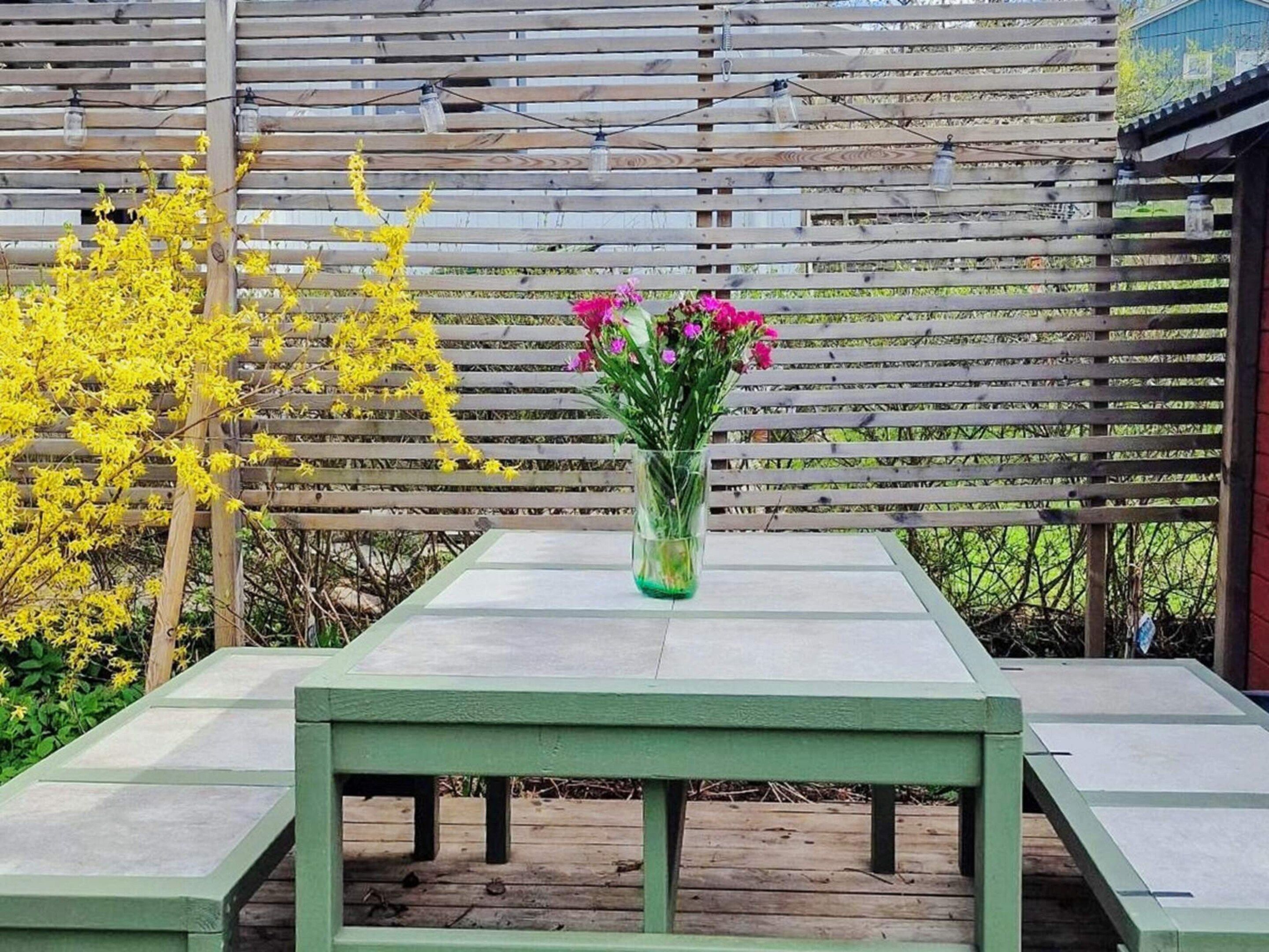 A wooden table with a vase of flowers in front of a wooden fence.