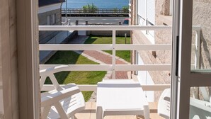 Ein Balkon mit weißen Stühlen und einem Tisch, der auf eine grüne Fläche und ein Gewässer blickt.