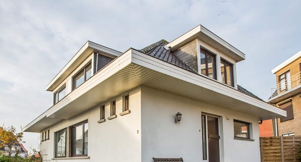 Een modern huis met twee verdiepingen, een plat dak, grote ramen en het cijfer '2' op de gevel.