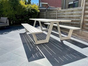 Een picknicktafel met een bank in een achtertuin met een betegeld terras en een houten omheining.
