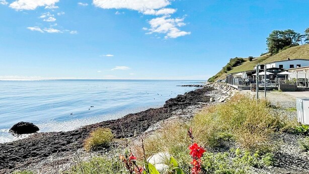 A coastal scene with a clear sky, a rocky shoreline, and a building with outdoor seating. - 4 Person Holiday Home in Hammenhog-by Traum (Hammenhög)