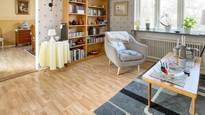 A cozy living room with a wooden floor, a bookshelf, a comfortable armchair, and a dining table with a placemat. - 4 Person Holiday Home in Hammenhog-by Traum (Hammenhög)