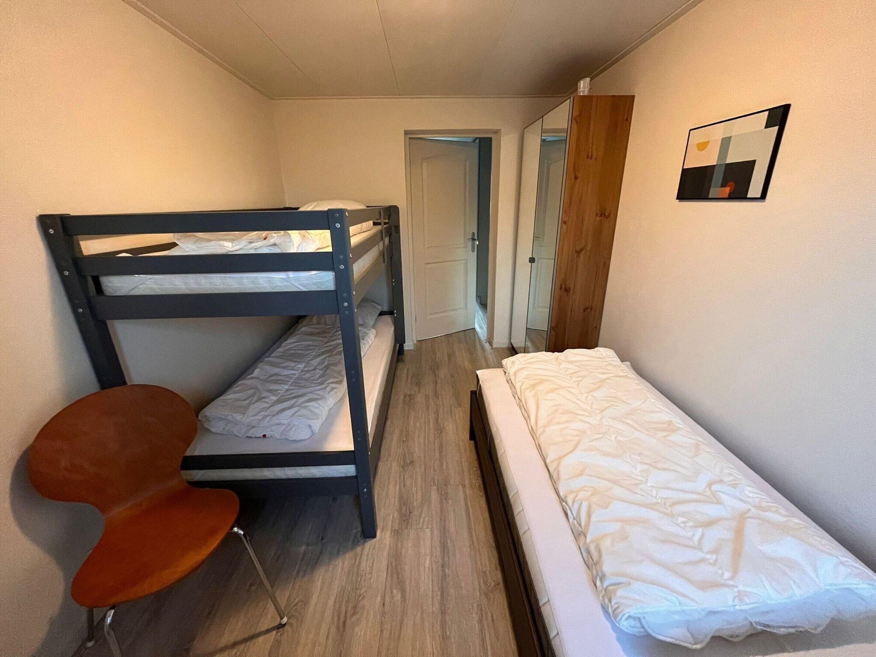 A narrow room with bunk beds, a single bed, a chair, and a mirror.