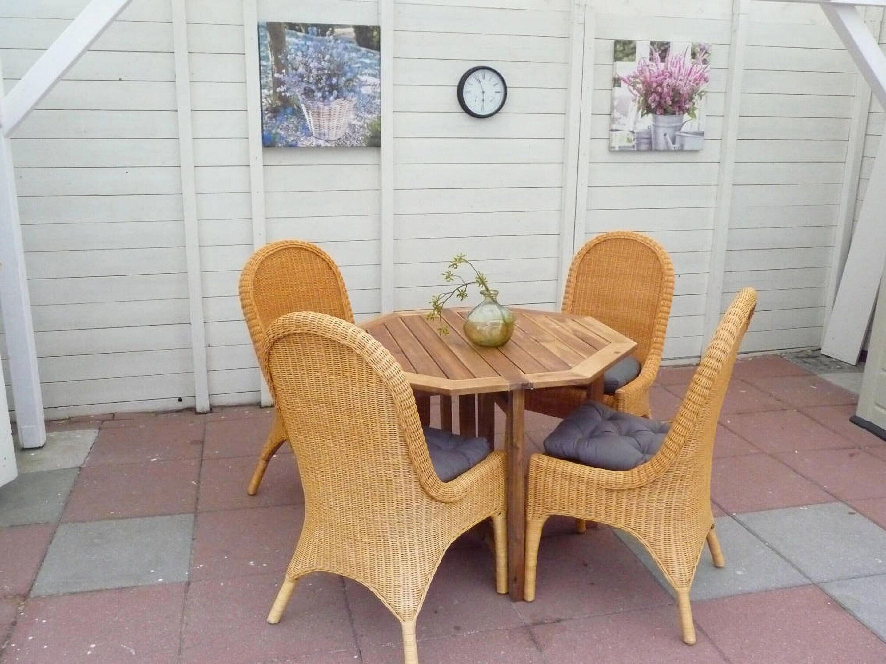 Een terras met een houten tafel en vier rieten stoelen met kussens.