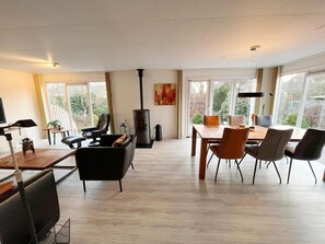 A modern living room with a fireplace, dining area, and large windows. - Bungalow in Makkum Near Lake Beach (Makkum)