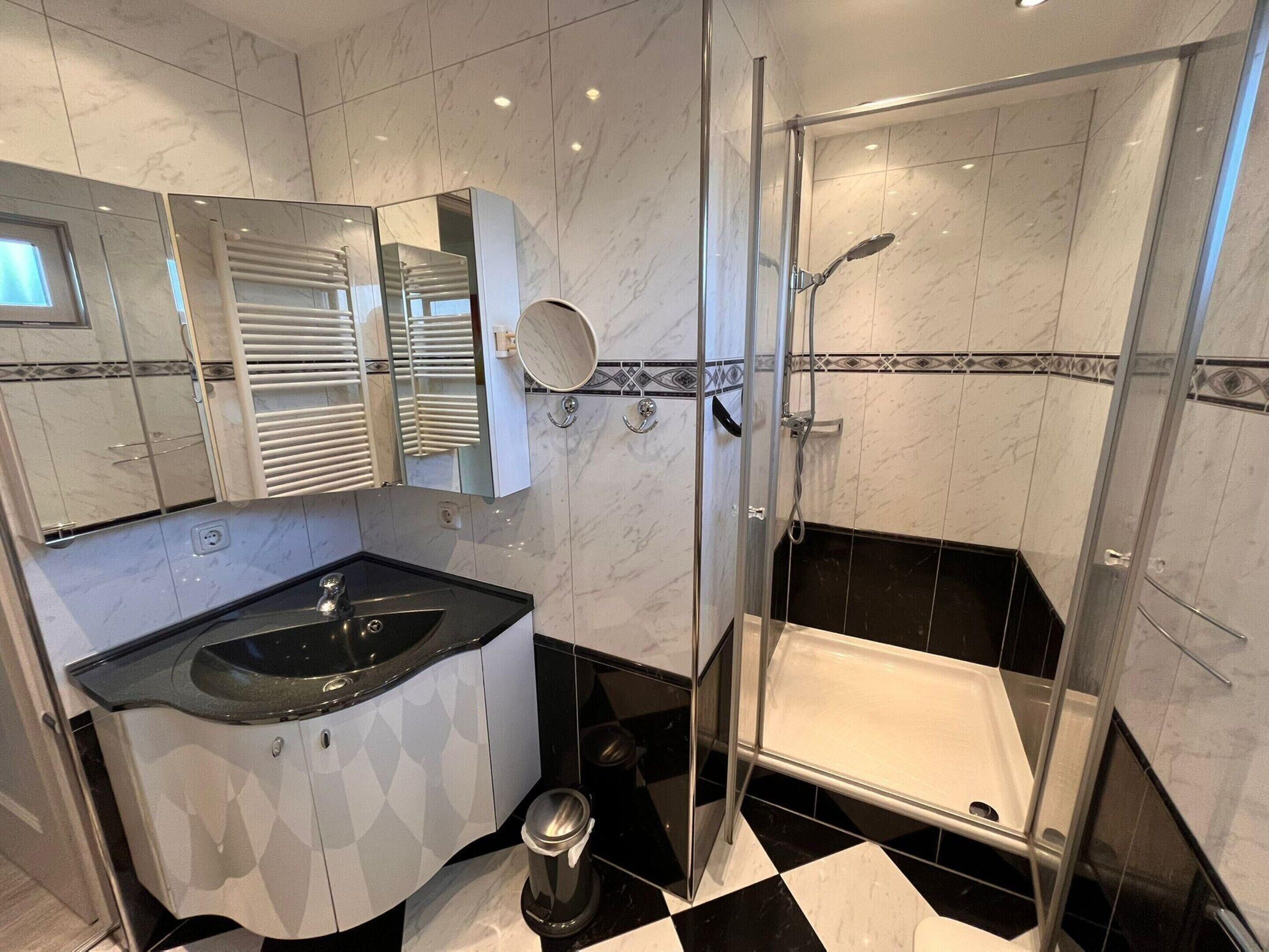 A modern bathroom with a black and white checkered floor, a white sink with a mirror above it, a shower with a glass door, and a toilet.