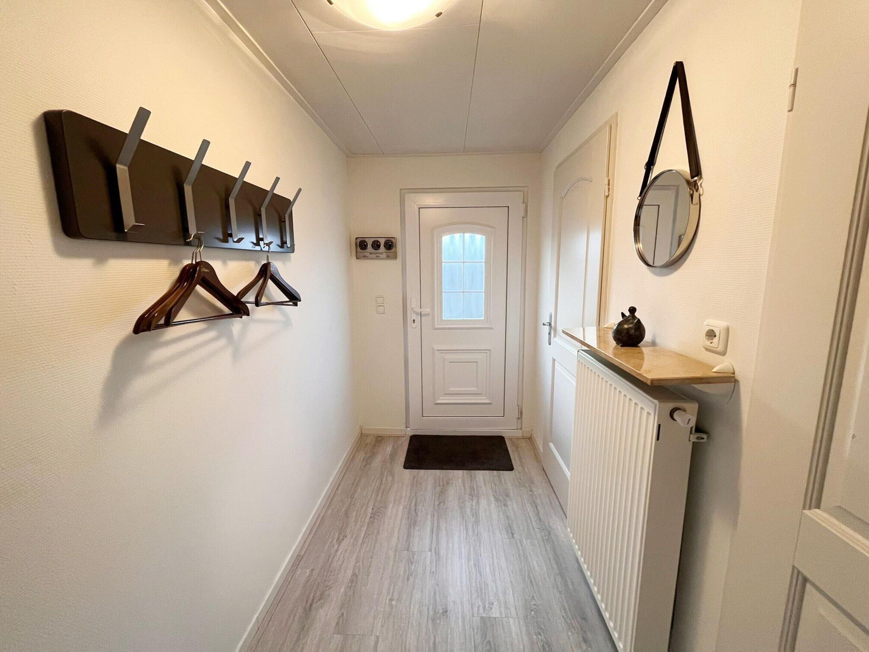 A hallway with a white door, a radiator, and a coat rack with hangers.