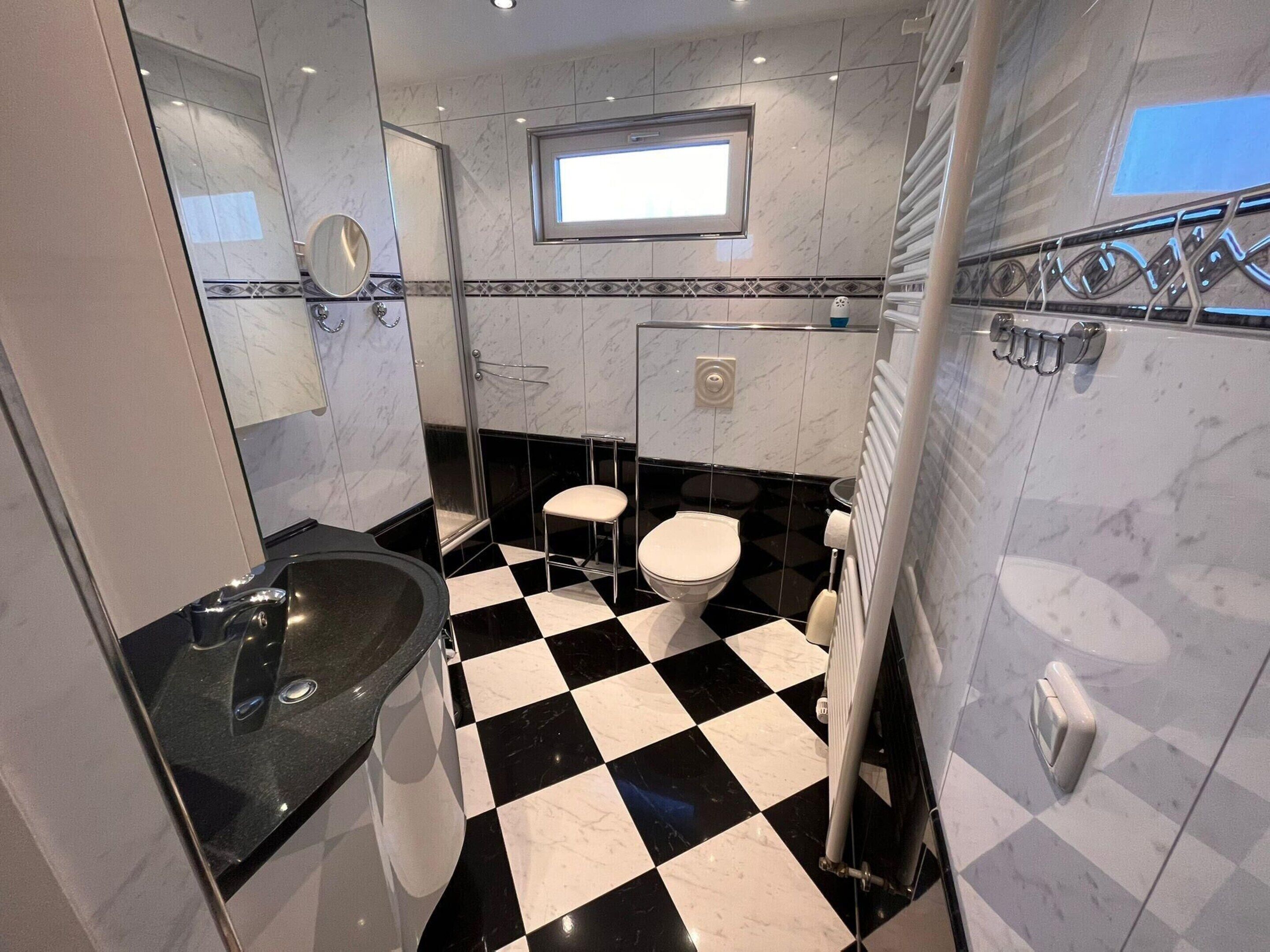 Un baño con piso a cuadros blancos y negros, un lavamanos, un inodoro y una zona de ducha.