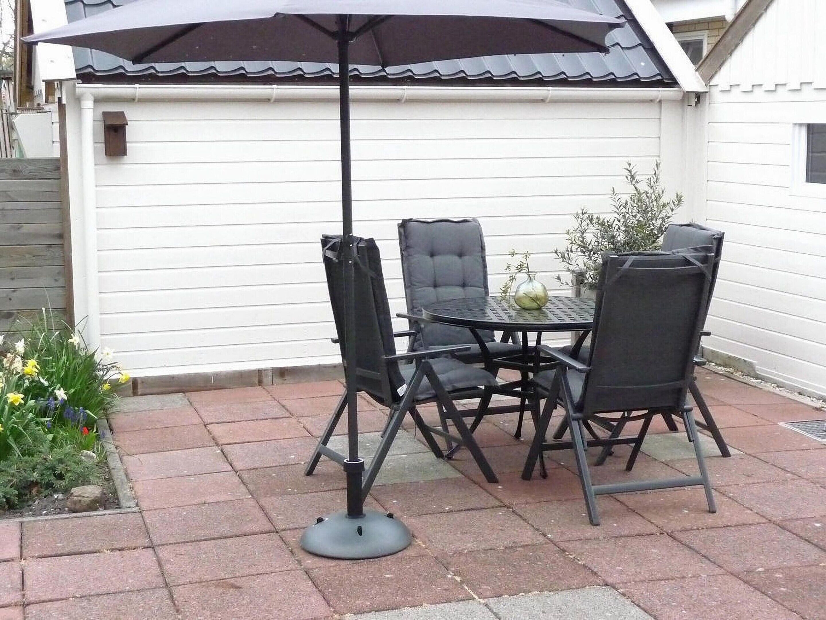 Un patio exterior con una mesa, cuatro sillas, una sombrilla y una planta en maceta.