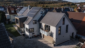 A modern house with solar panels on the roof, a paved courtyard, and a view of surrounding houses and hills. - Holiday Apartment Swallow's Nest (Eichstetten am Kaiserstuhl)