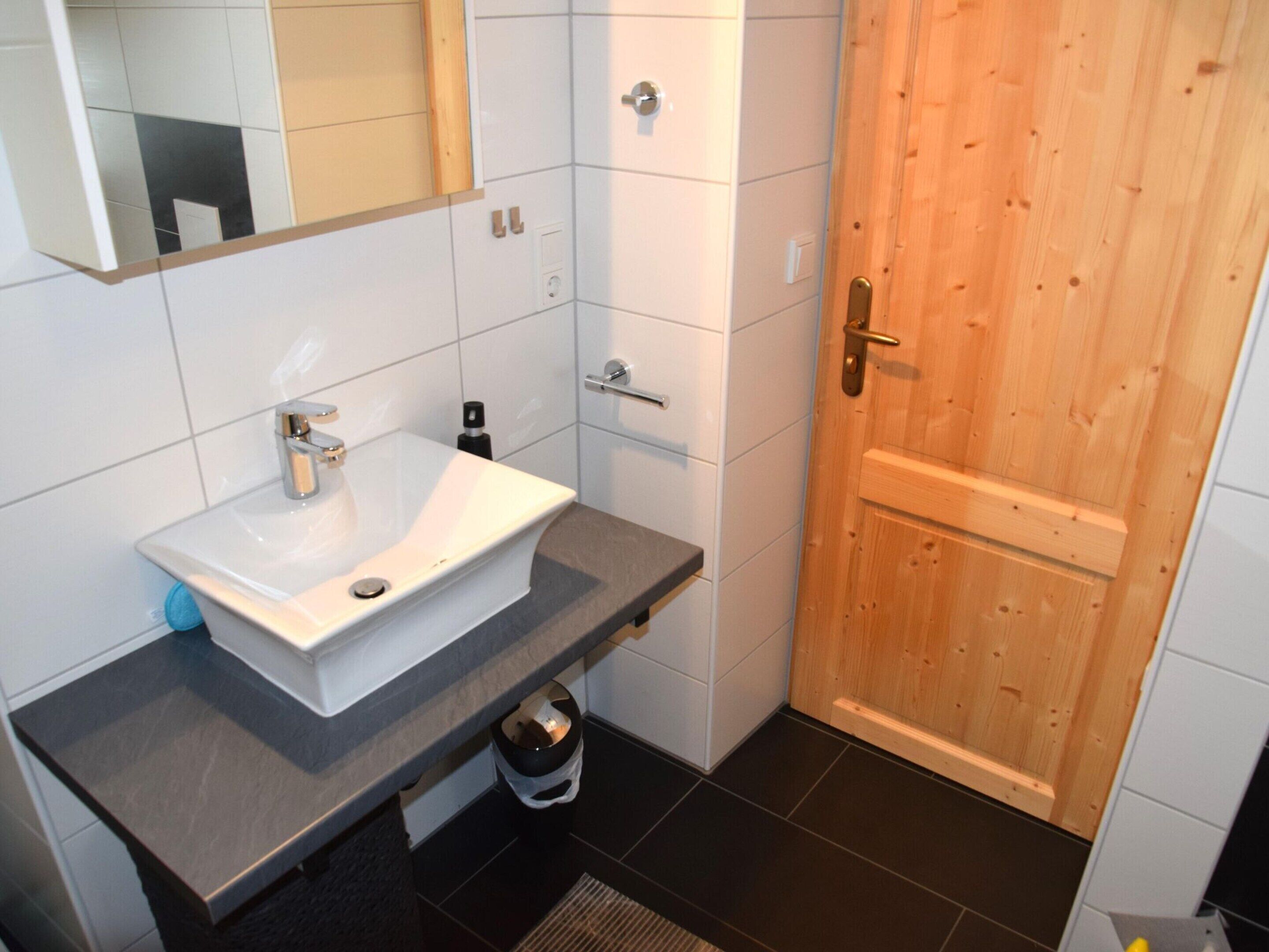 A bathroom with a white sink, dark countertop, and a wooden door.