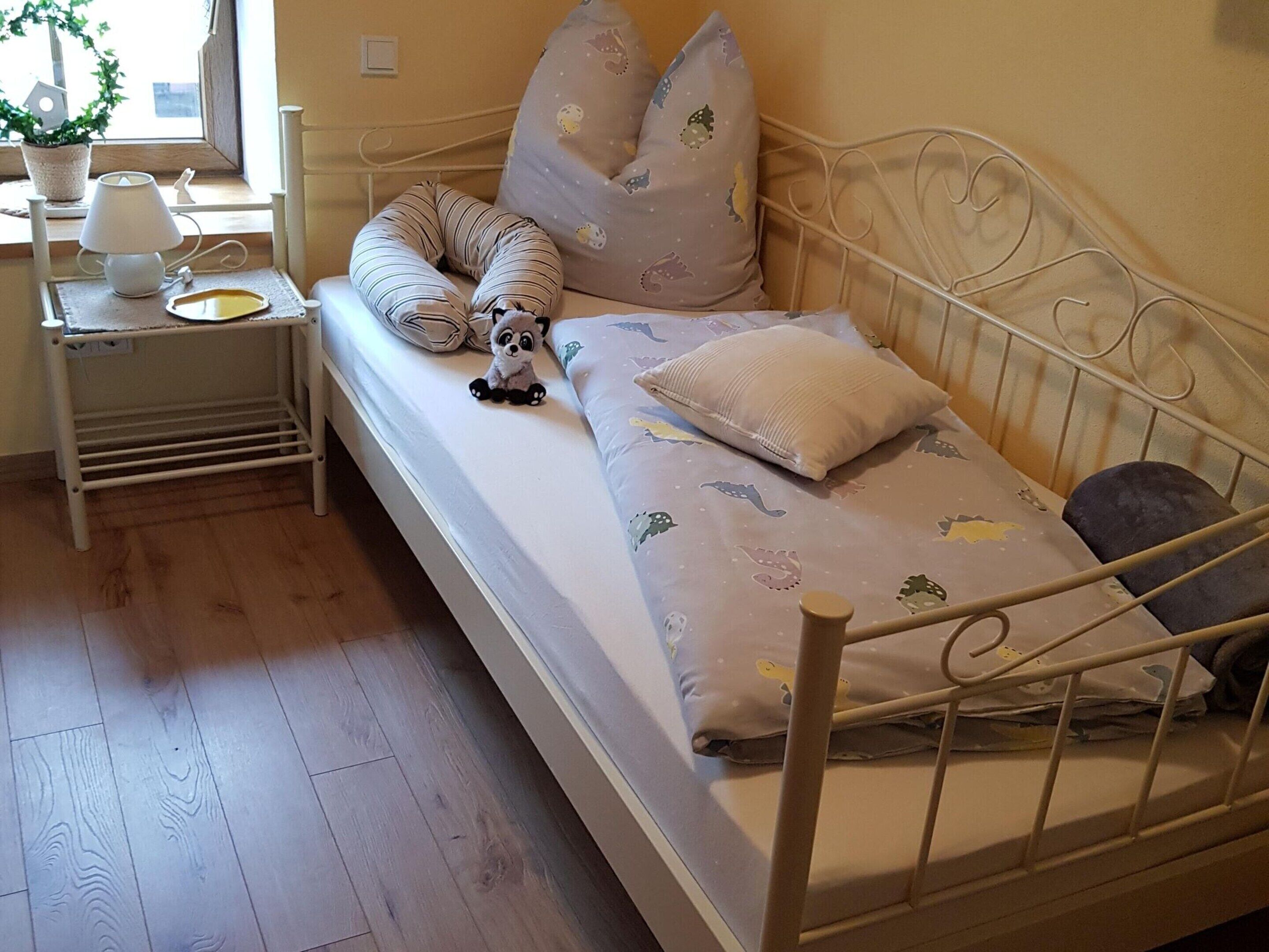 En säng för en person med en metallram, ett sängbord med en lampa och ett fönster med en växt.