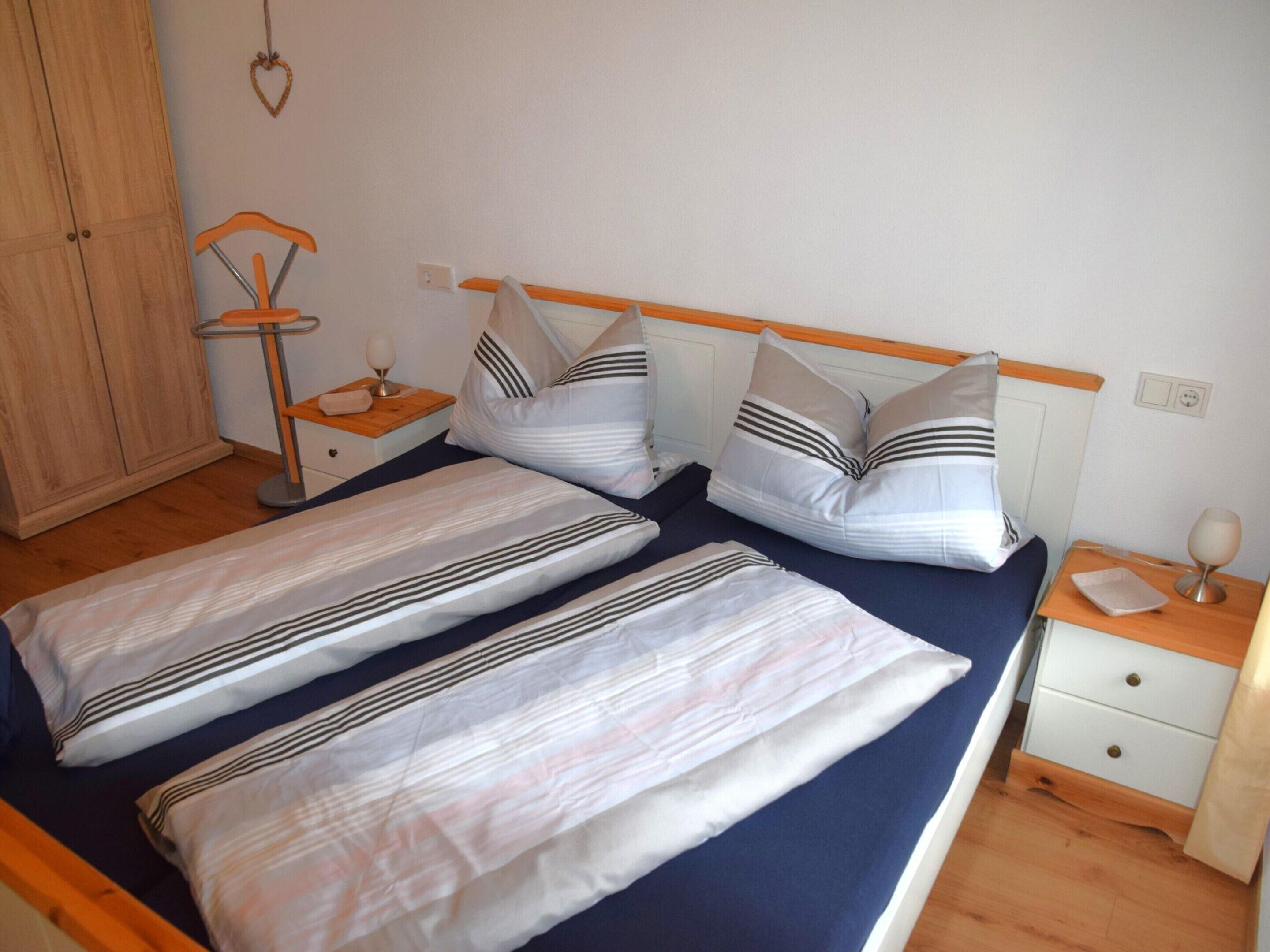 A double bed with striped bedding, a bedside table with a lamp, and a wooden wardrobe.