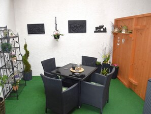 A patio area with a table and chairs, surrounded by potted plants and wall art.