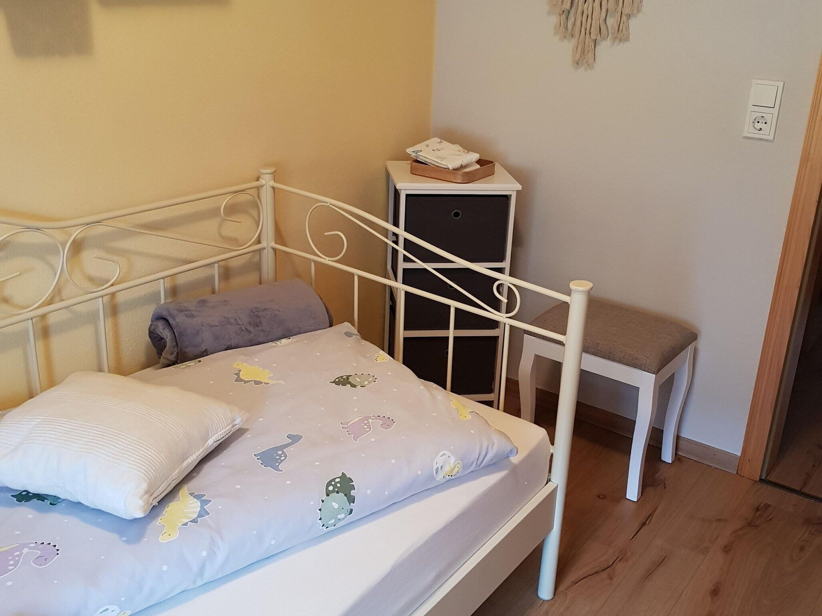 A small, neatly arranged bedroom with a single bed, a bedside table, and a small cabinet.