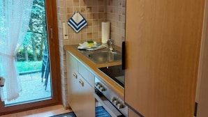 Une cuisine de taille réduite, dotée de meubles de rangement en bois, d’un four encastré et d’un évier.