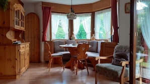 Une pièce chaleureuse avec un buffet en bois, une table à manger avec des chaises, un banc et de grandes fenêtres avec des rideaux.