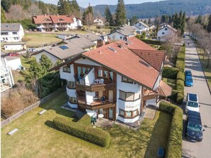 A two-story house with a balcony, a fenced yard, and a driveway with parked cars. - Barenhusli No. 2 Comfortable Holiday Residence (Titisee-Neustadt)