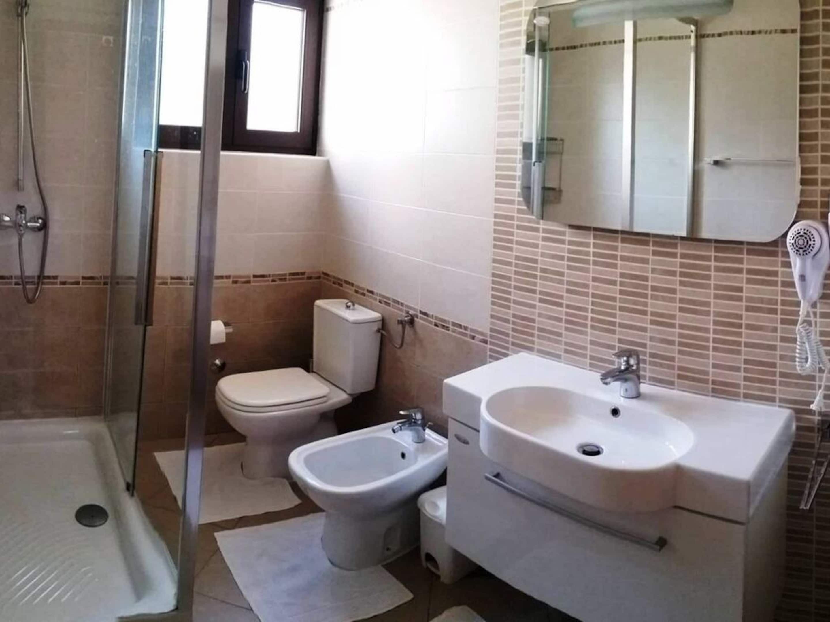 Ein Badezimmer mit Glasdusche, Toilette, Bidet, Waschbecken und einem Spiegel darüber.