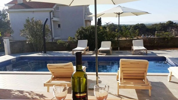 A poolside area with a wooden table, two lounge chairs, and a bottle of wine. - Mesmerising Apartment in Punat (Punat)