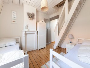 A bedroom with two beds, a wardrobe, a small table, a lamp, and a staircase.