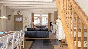 A spacious living area with a high ceiling, a wooden staircase, a dining area with a table and chairs, and a sofa. - Seaside Charm & Privacy (Nieuwpoort)