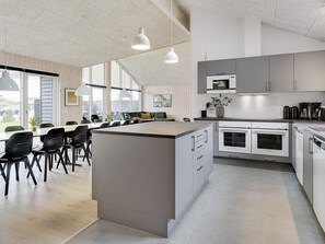 A modern kitchen with a central island, white cabinetry, and a dining area with black chairs. - 5 Star Holiday Home in Albaek (Aalbaek)