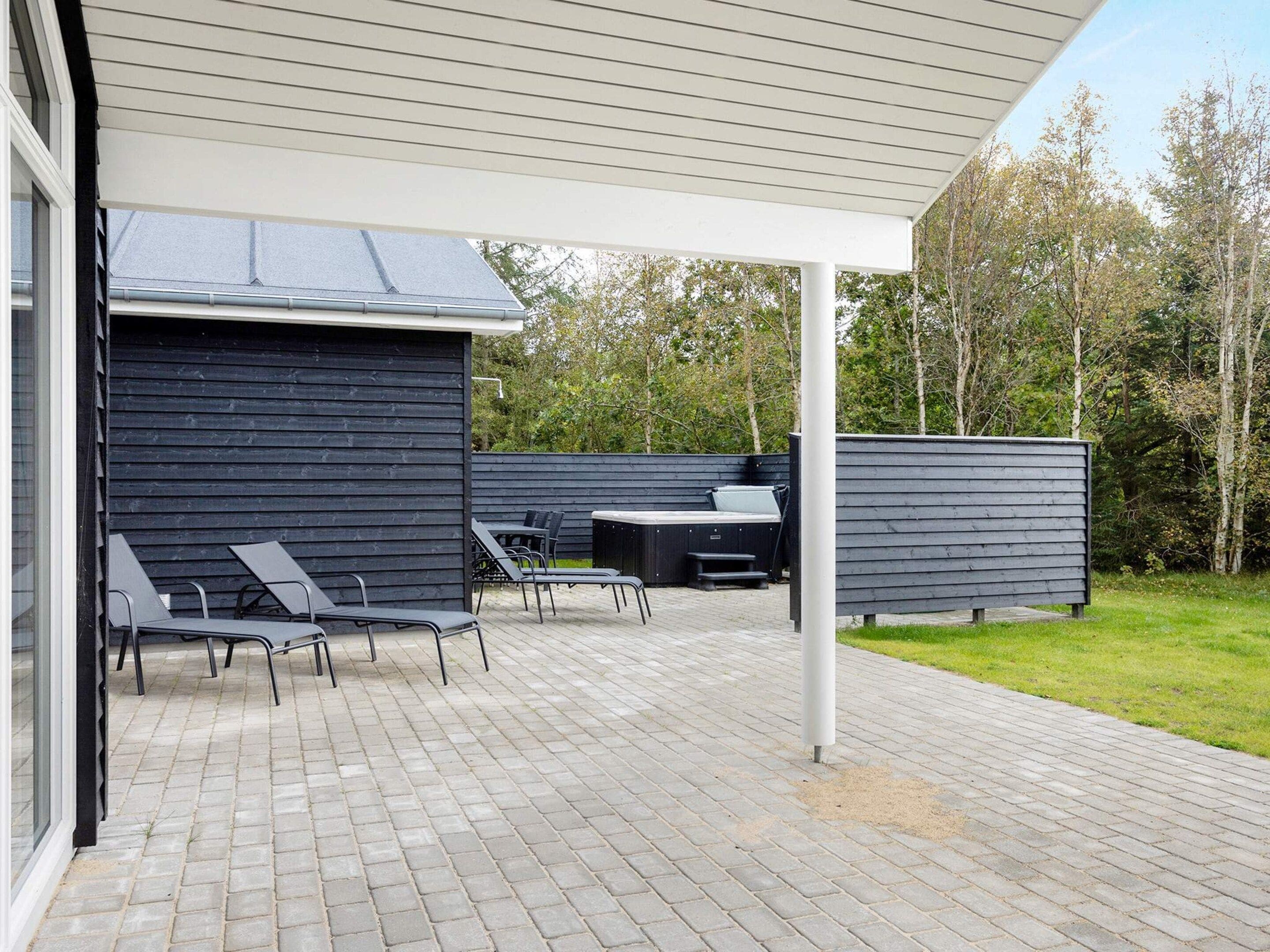 An outdoor patio with a covered seating area, a hot tub, and a barbecue grill.