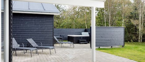 An outdoor patio with a covered seating area, a hot tub, and a barbecue grill.