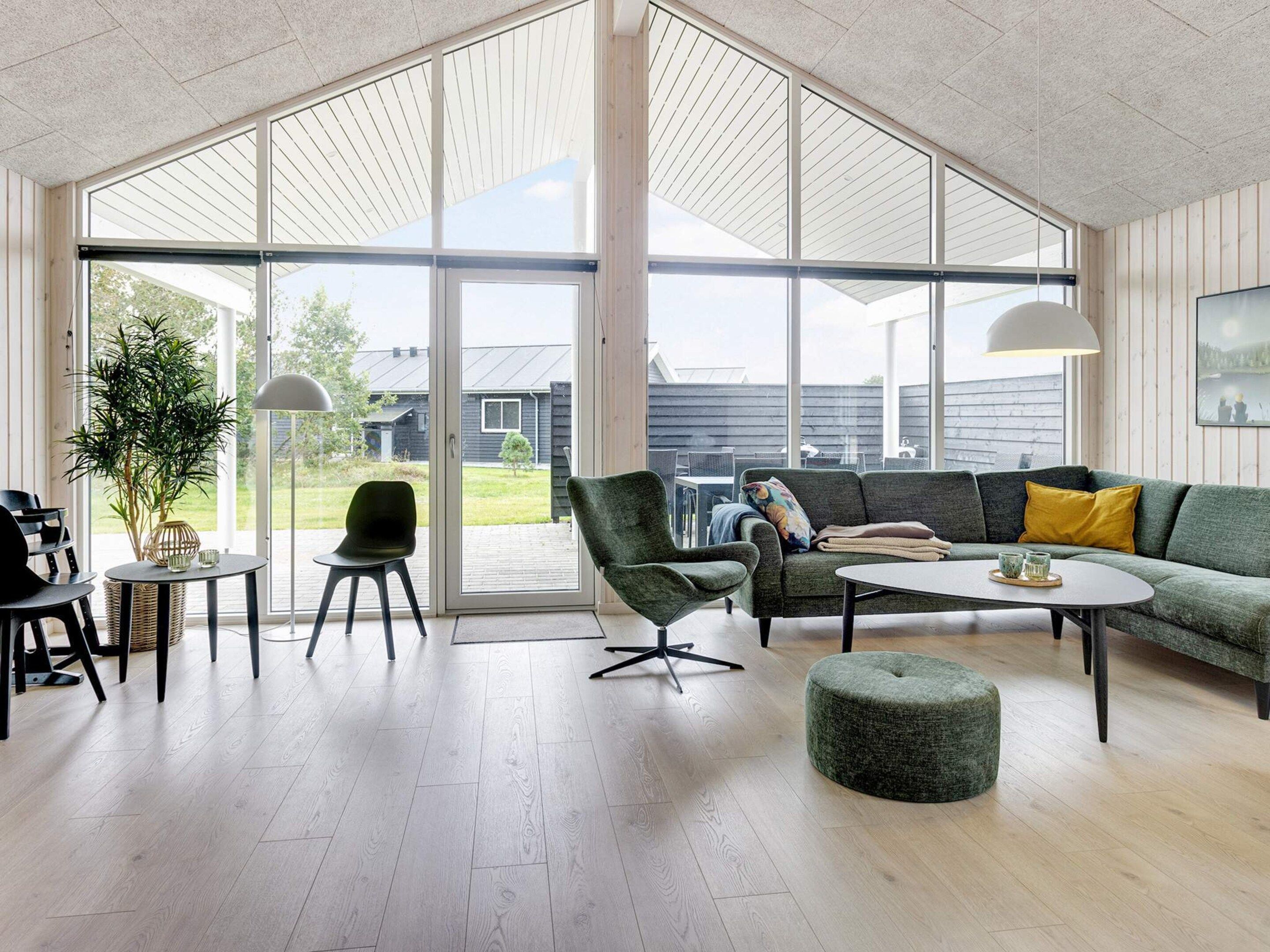 A modern living room with a large glass door leading to an outdoor area, a green sofa, a round ottoman, and a small table with decorative items.