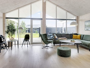 A modern living room with a large glass door leading to an outdoor area, a green sofa, a round ottoman, and a small table with decorative items. - 5 Star Holiday Home in Albaek (Aalbaek)
