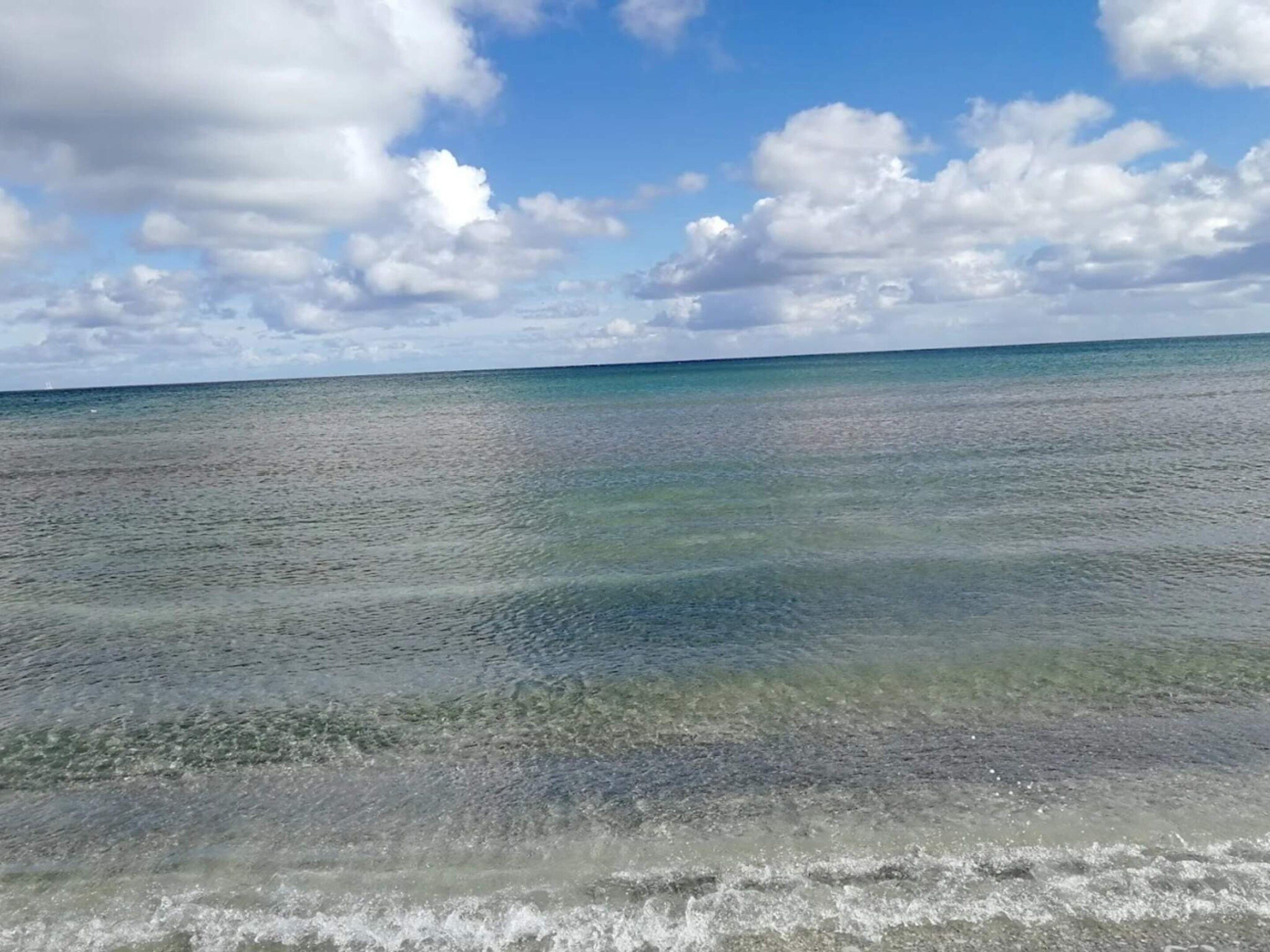 On aperçoit clairement une plage avec une eau calme et un ciel partiellement nuageux.