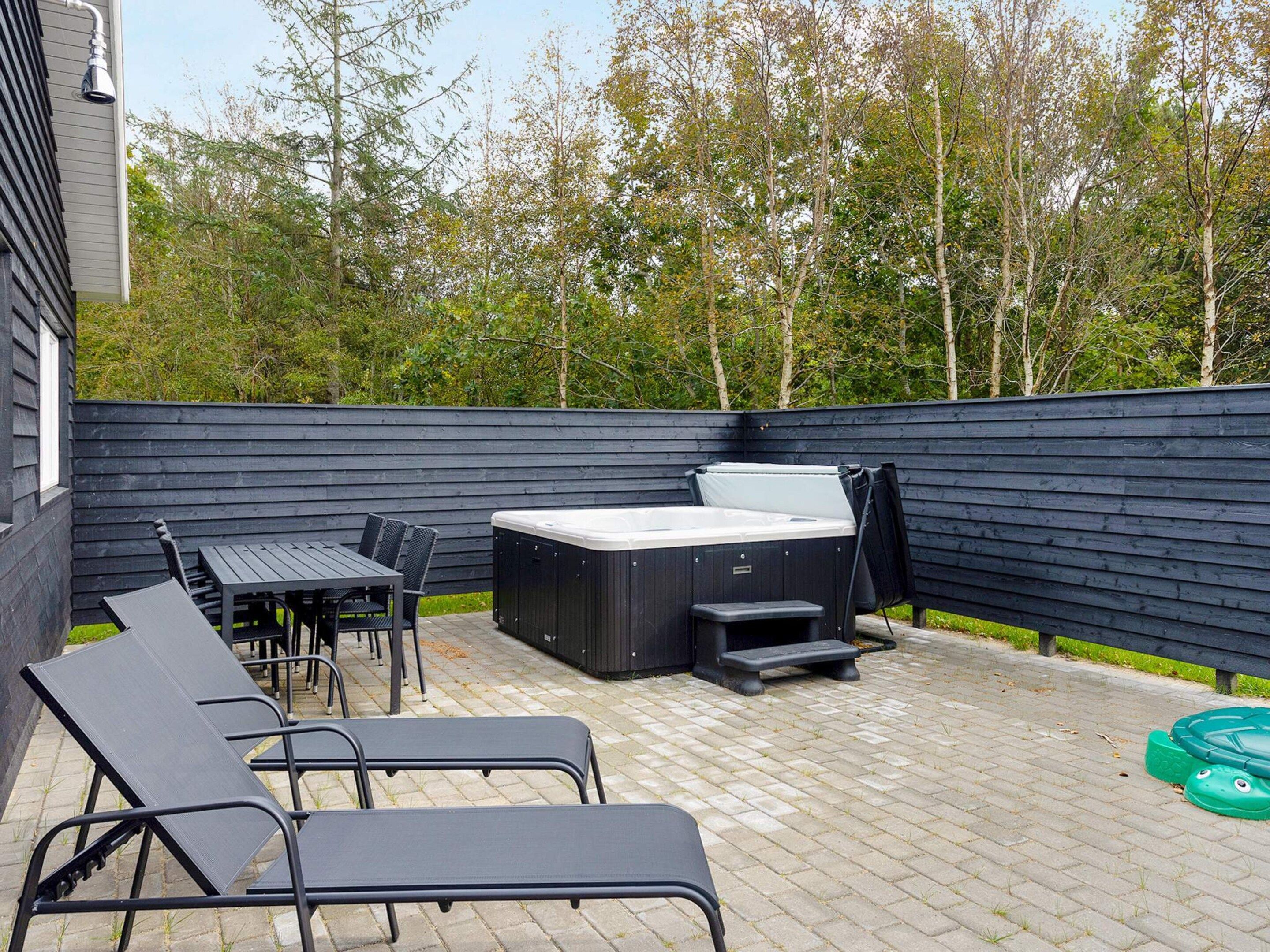 An outdoor patio with a hot tub, lounge chairs, and a table.