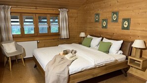 Un dormitorio de cabaña de madera con una cama, dos mesitas de noche, una silla y un ventanal con cortinas.