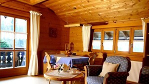 Interior acogedor de una cabaña con paredes y techo de madera, un comedor con mesa y sillas, y una sala de estar con una mesa redonda y sillones.