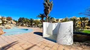 A pool area with tiled flooring, a small pool, and palm trees. - Apartment in Roquetas Near the Beach (Roquetas de Mar)