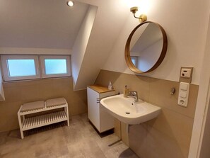 A modern bathroom with a skylight, a freestanding sink, a vanity, and a bench.