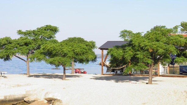 A beach with trees, a gazebo, and a building by the water. - Sunny Pool Apartments - One Bedroom Apartment (Jasenice)