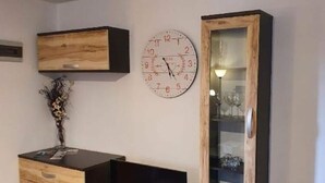 A room with a wooden TV stand, a wall clock, and a cabinet with glass doors. - Sunny Pool Apartments - One Bedroom Apartment (Jasenice)