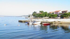 A coastal scene with boats docked near a pier, surrounded by residential buildings and greenery. - Sunny Pool Apartments - One Bedroom Apartment (Jasenice)