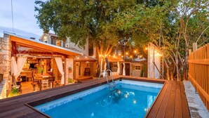 A rectangular swimming pool with a wooden deck, surrounded by a wooden fence and trees. - Vakantiehuis Loris (Marcana)