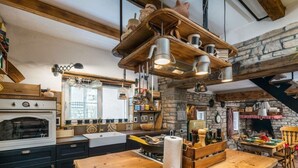 A rustic kitchen with a stone wall, wooden beams, and a hanging light fixture. - Vakantiehuis Loris (Marcana)