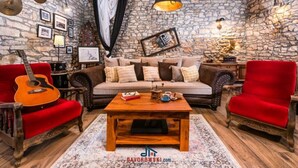 A rustic living room with a stone wall, wooden ceiling beams, a red sofa, a wooden coffee table, and a guitar. - Vakantiehuis Loris (Marcana)