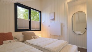 Une chambre avec deux lits, une fenêtre avec des stores, un radiateur fixé au mur, un miroir et un tableau encadré.