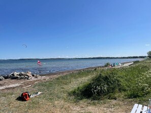 Une vue sur le lac, avec un ciel dégagé, une plage de sable et un voilier à l’horizon.