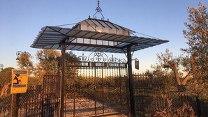 A gated entrance with a pergola structure, a metal gate, and a sign indicating a connection to a nearby location. - Holiday Home Between Mountain, Coast (Bollullos Par del Condado)