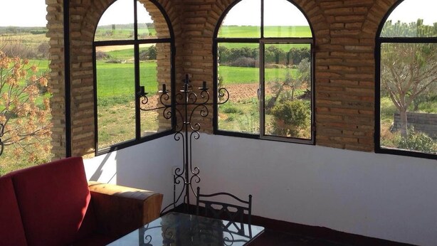 A room with a glass table and chairs, a red sofa, and three arched windows offering a view of a green landscape. - Holiday Home Between Mountain, Coast (Bollullos Par del Condado)