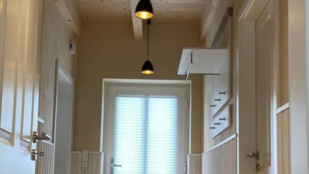 Een hal met een bank, houten plafond en een deur met raam.