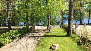 A park pathway leading to a lake, surrounded by trees and a fence.