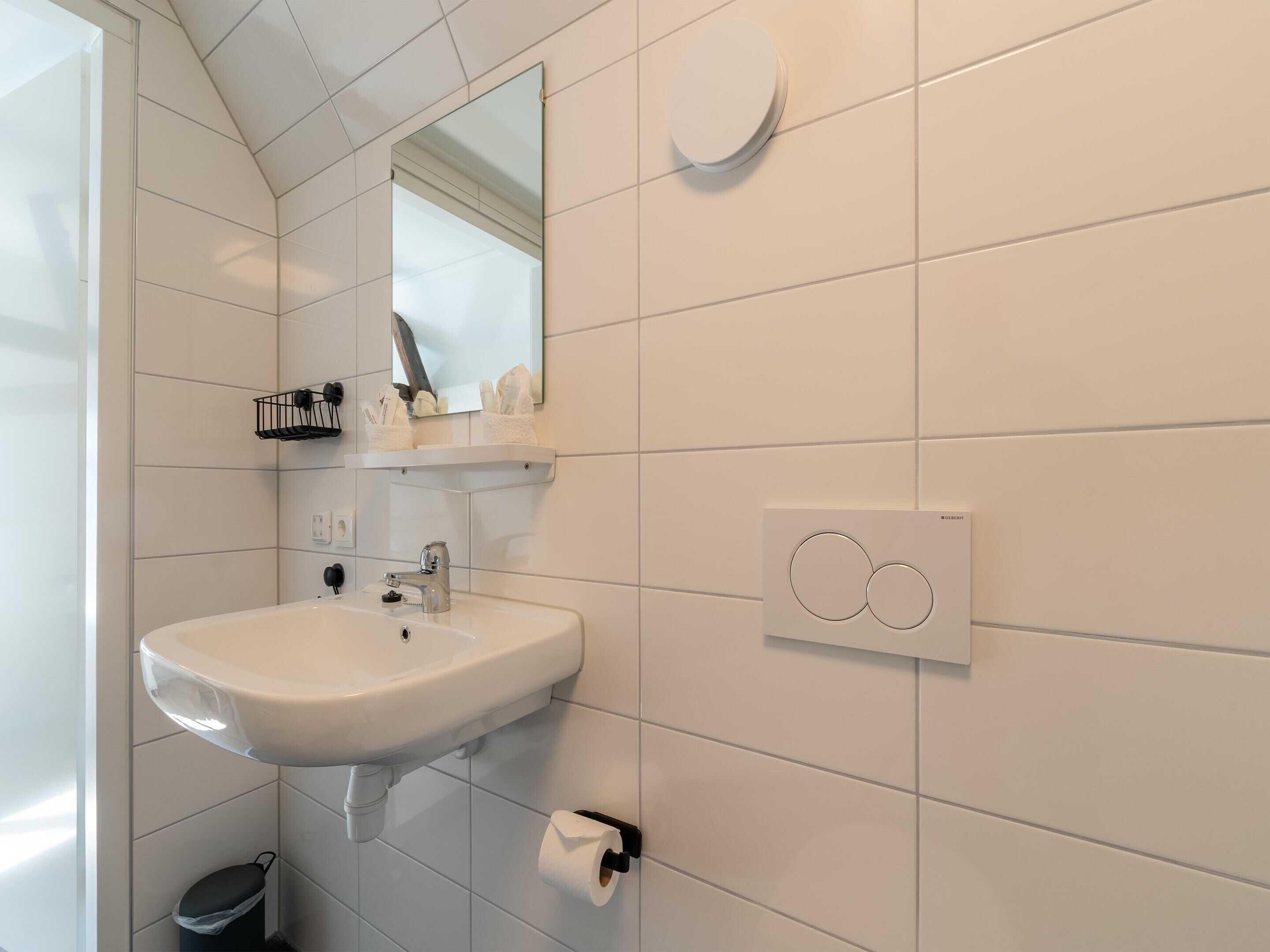 Une salle de bain moderne avec un lavabo blanc, un miroir et un porte-rouleau de papier toilette.